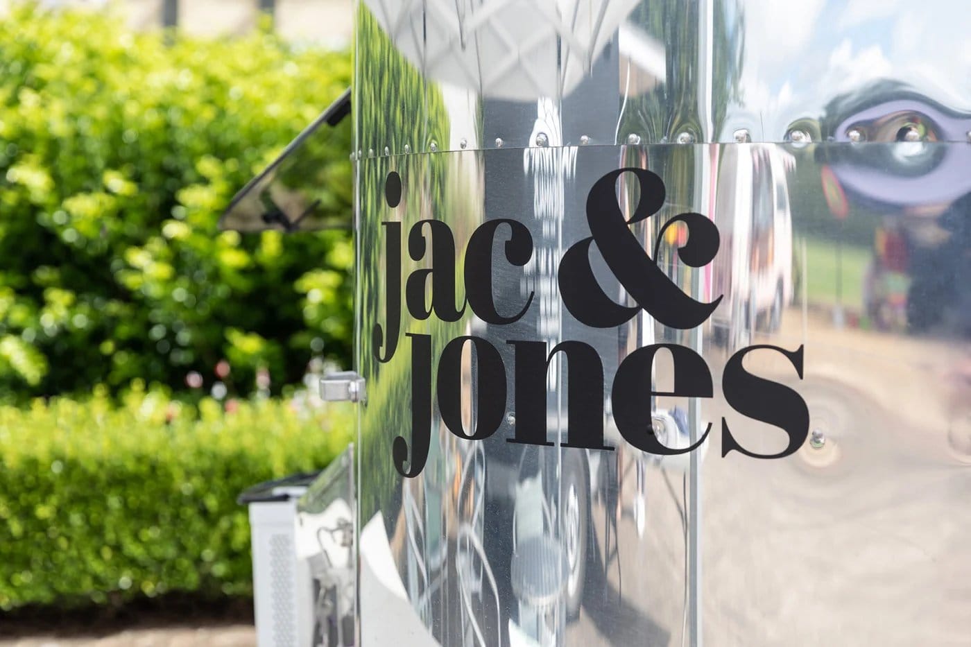 Jac and Jones signage on exterior wall with vineyard and garden trees