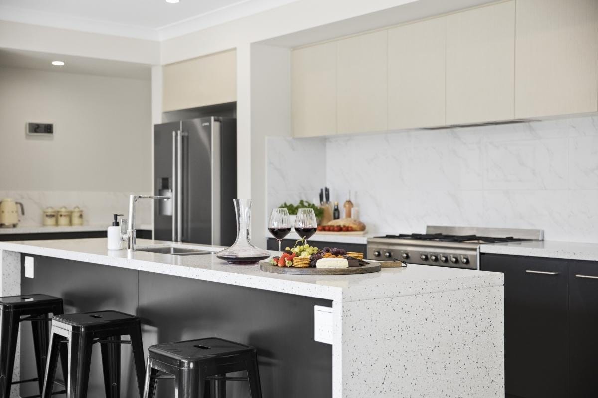 Open-plan kitchen island with wine glasses and a cheese board, dining table and living area beyond.