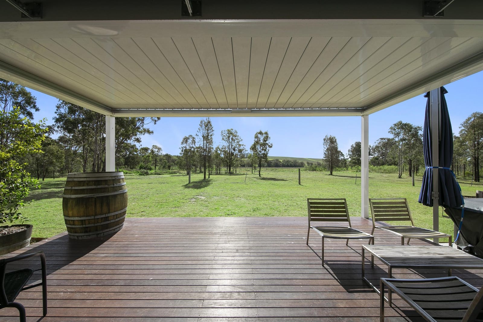 Covered timber deck with a wine barrel and loungers, looking out over open paddock.