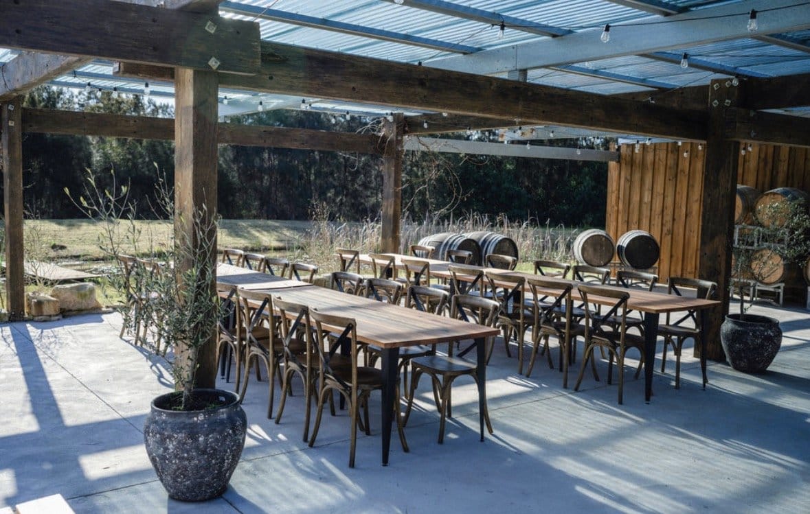 Covered outdoor dining terrace with timber tables and wine barrels at La Vigna Estate