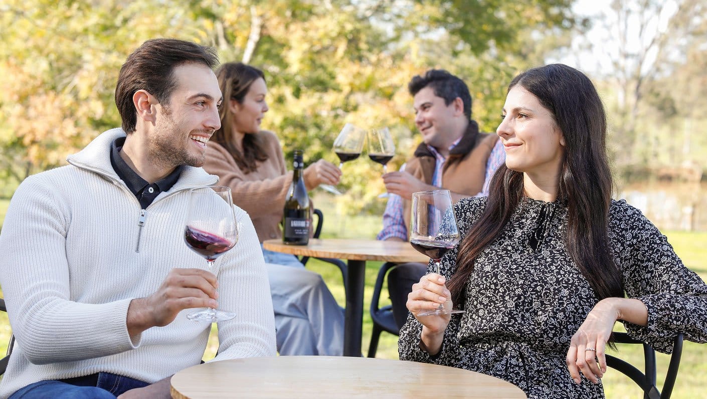 Group of friends enjoying wine together at outdoor vineyard dining table