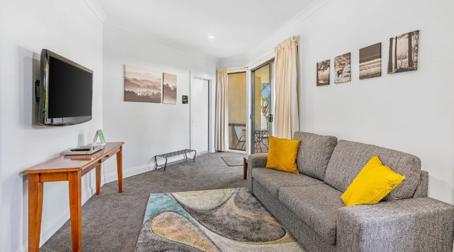 The lounge of a one-bedroom apartment with a sofa, television and sliding door to a private patio