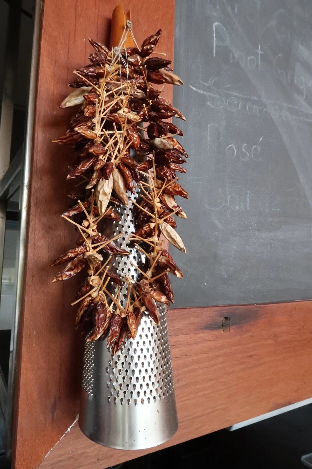 Dried chillies hanging from a cheese grater against a wall with a chalkboard wine list at Lillino's Bar and Trattoria