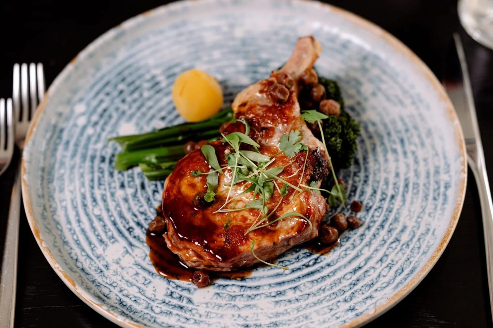Roasted pork cutlet with charred greens, jus and a boiled potato, plated at Locavore Restaurant.
