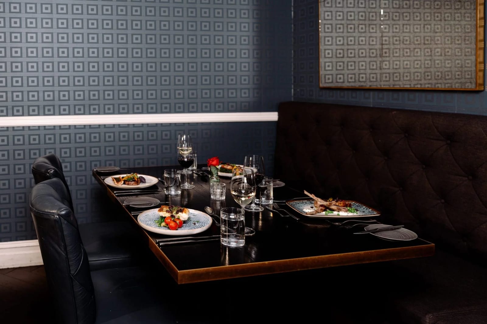 Corner table at Locavore Restaurant against patterned wallpaper, set with four plated courses and wine glasses.