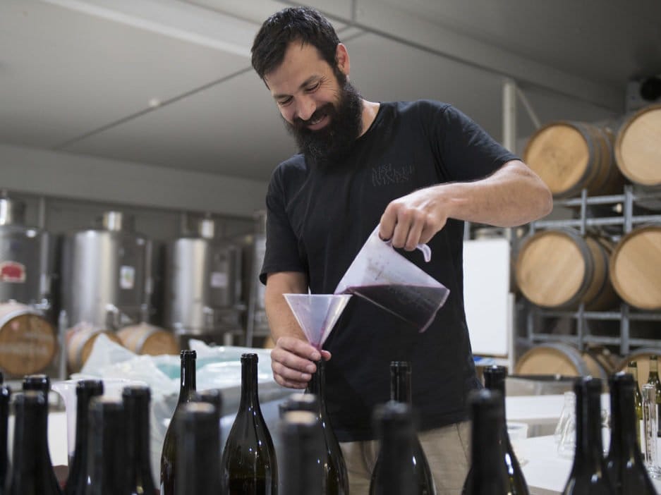 Winemaker pouring wine in production space with barrel storage