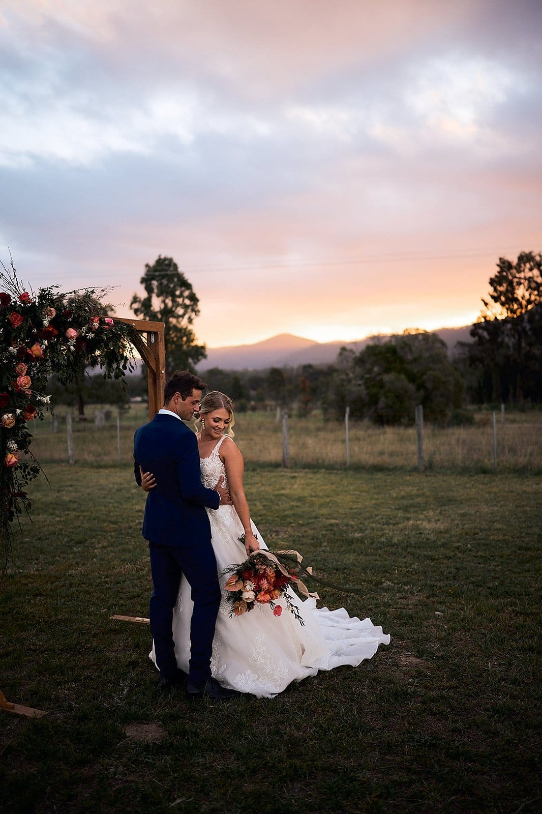 A couple in front of a floral arch on the paddock at sunset