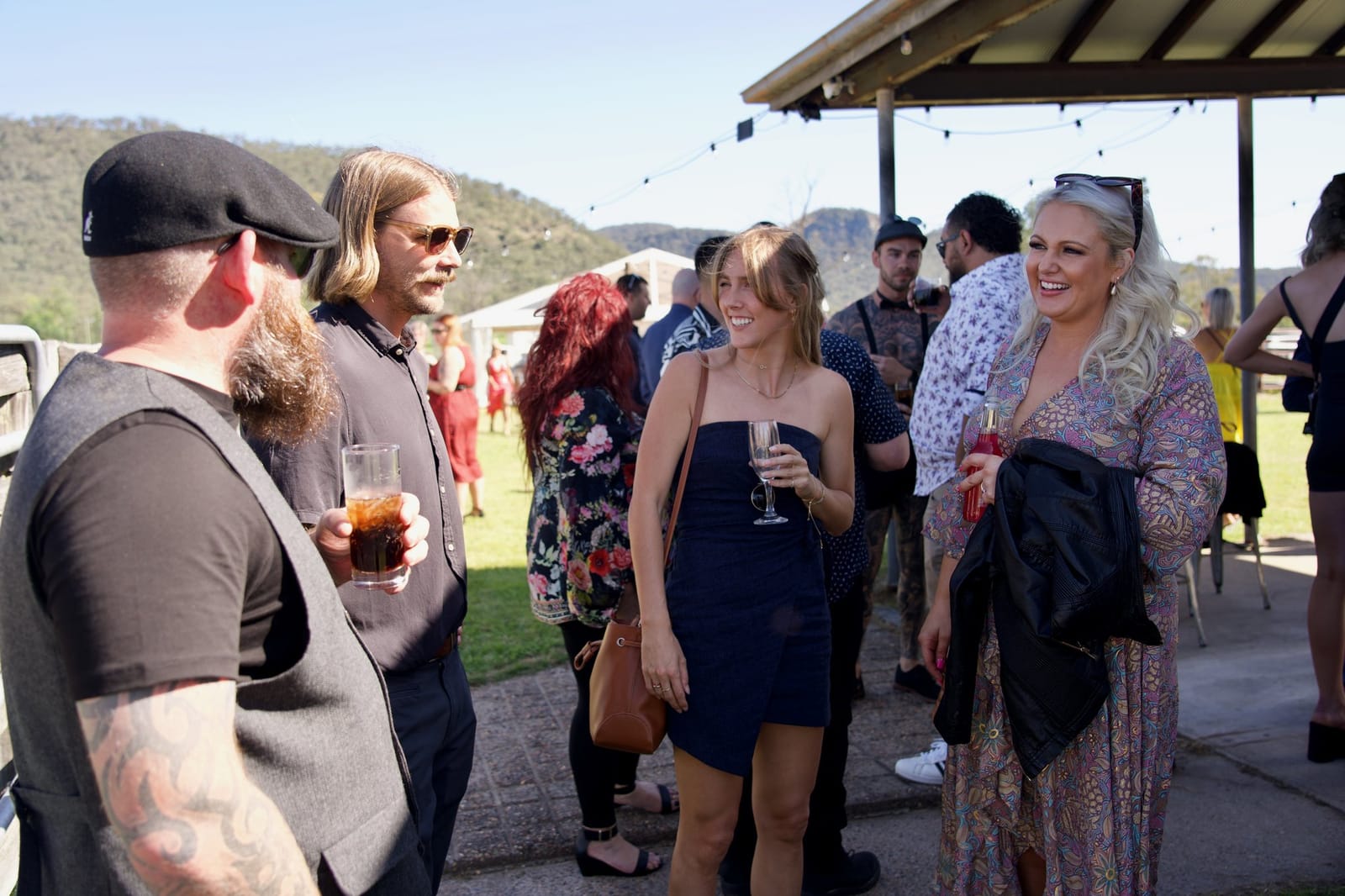 Guests with drinks under the open shed in daylight, ranges rising behind
