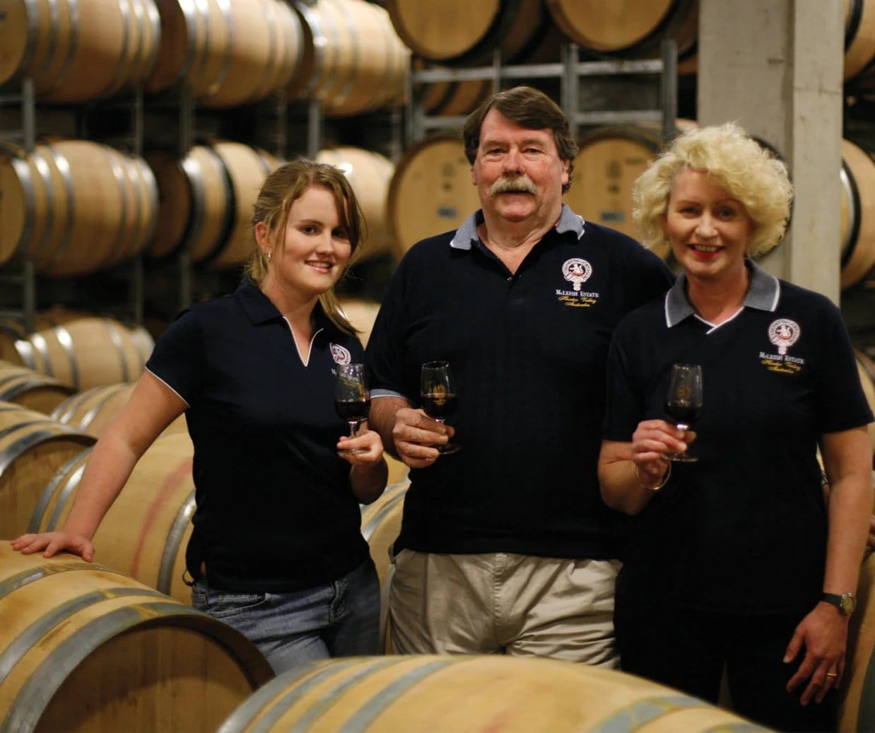 Winery team members with wine glasses in oak barrel cellar room
