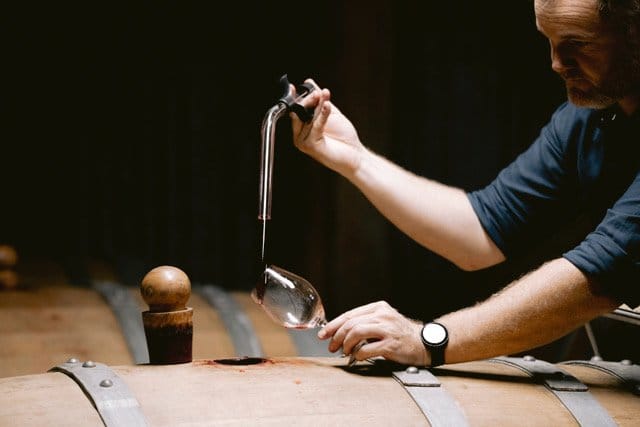 Winemaker drawing wine from wooden barrel using tap