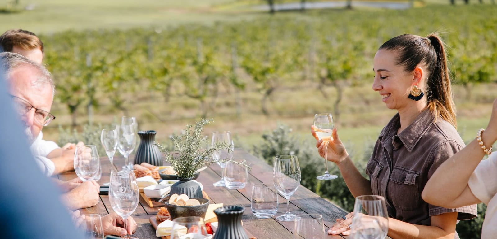 Guests tasting at the outdoor table with rows of vines in the background