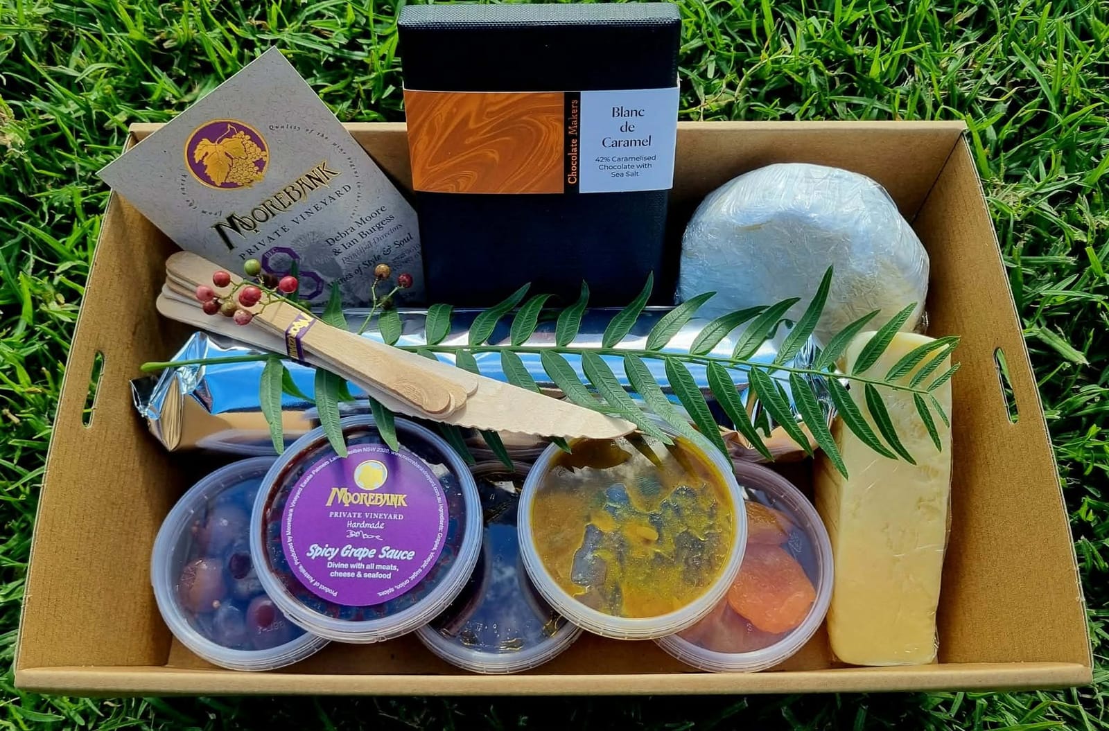 Gourmet picnic hamper with wine, sauces and chocolate on grass