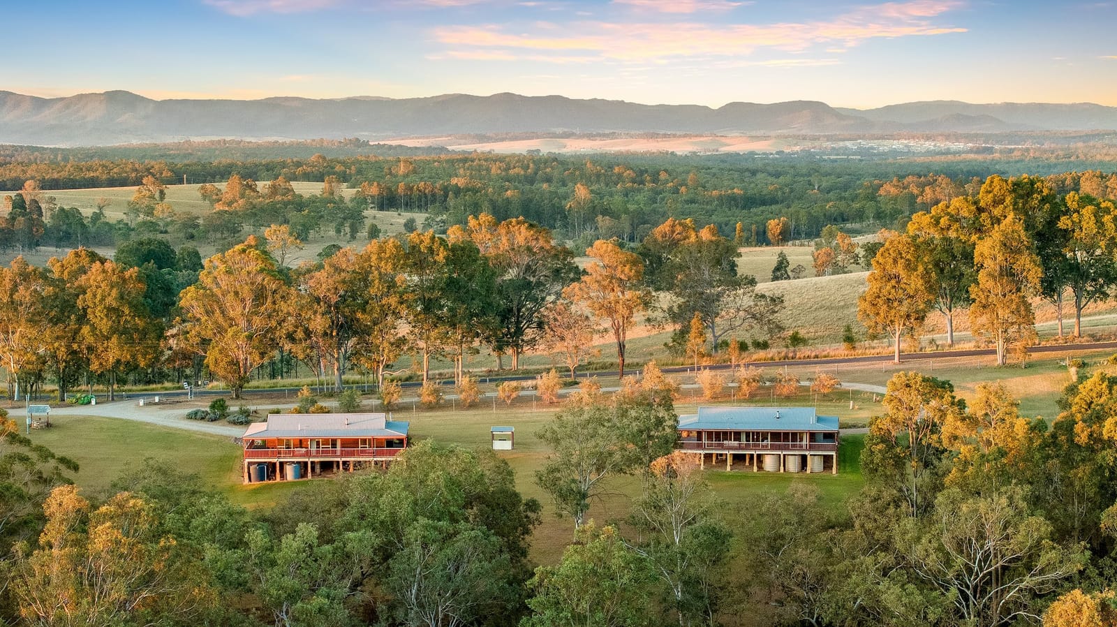 Aerial view of the two North Lodge cottages among trees with the Brokenback Range behind, Pokolbin