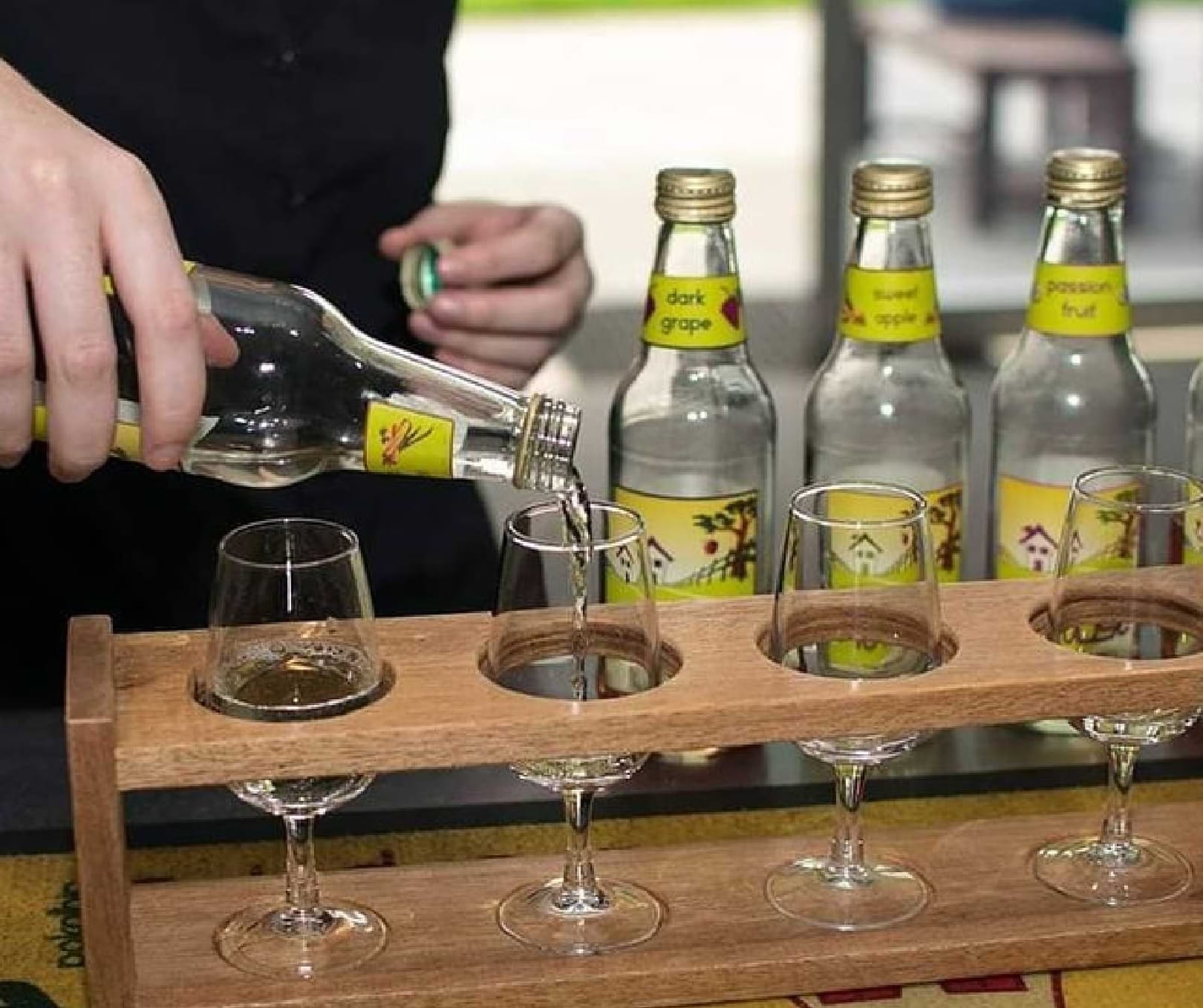 Cider being poured into a wooden tasting paddle beside labelled bottles