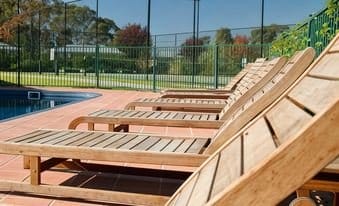 Sun loungers beside the outdoor pool, with the tennis court behind