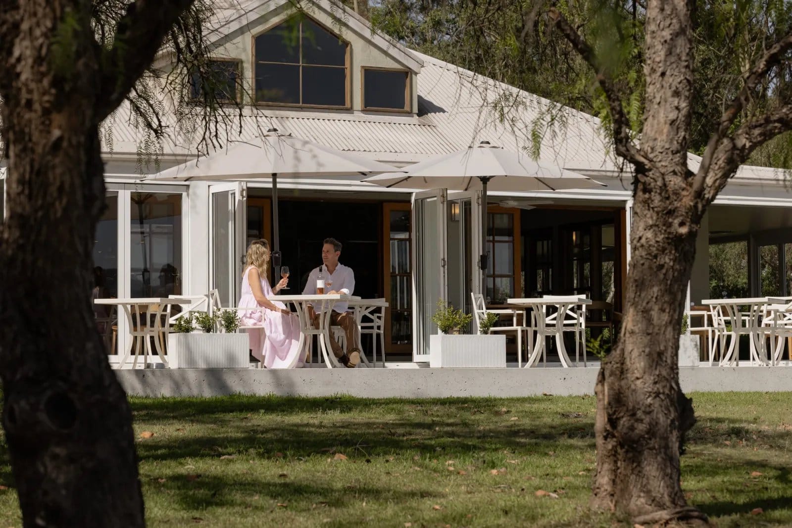 A couple with wine at an outdoor table on the Botanica terrace, framed by trees
