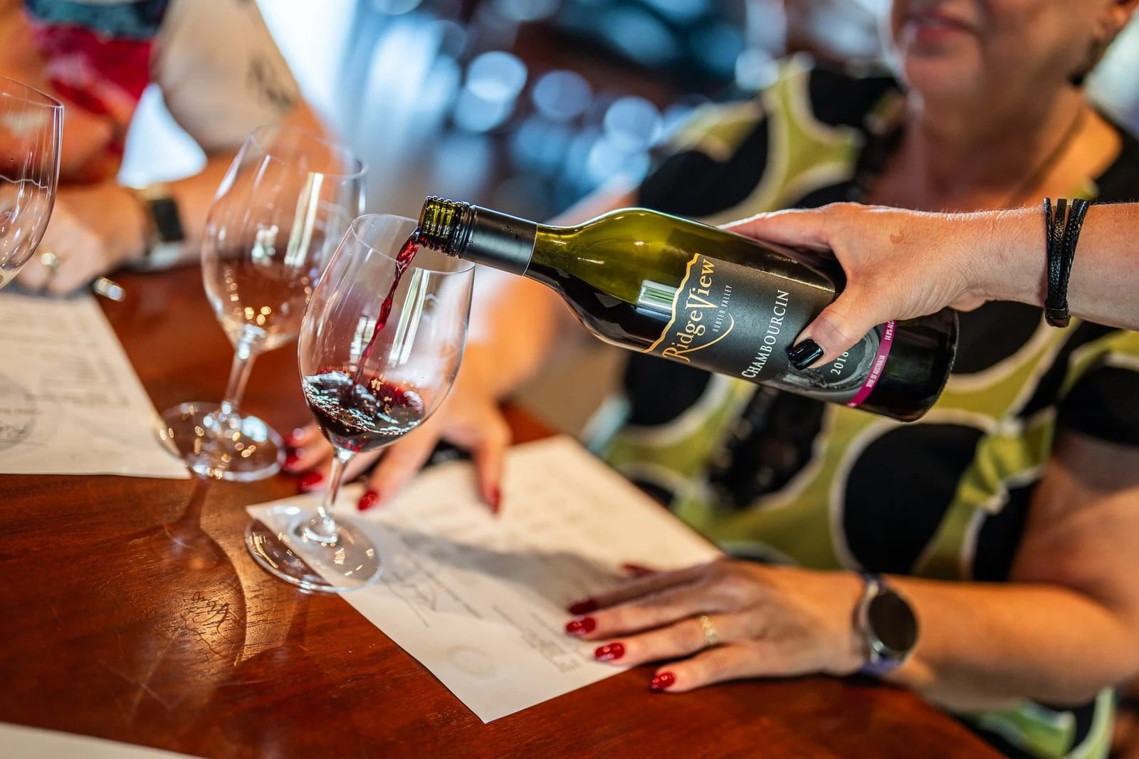 Red wine being poured during tasting with comparison glasses on bar