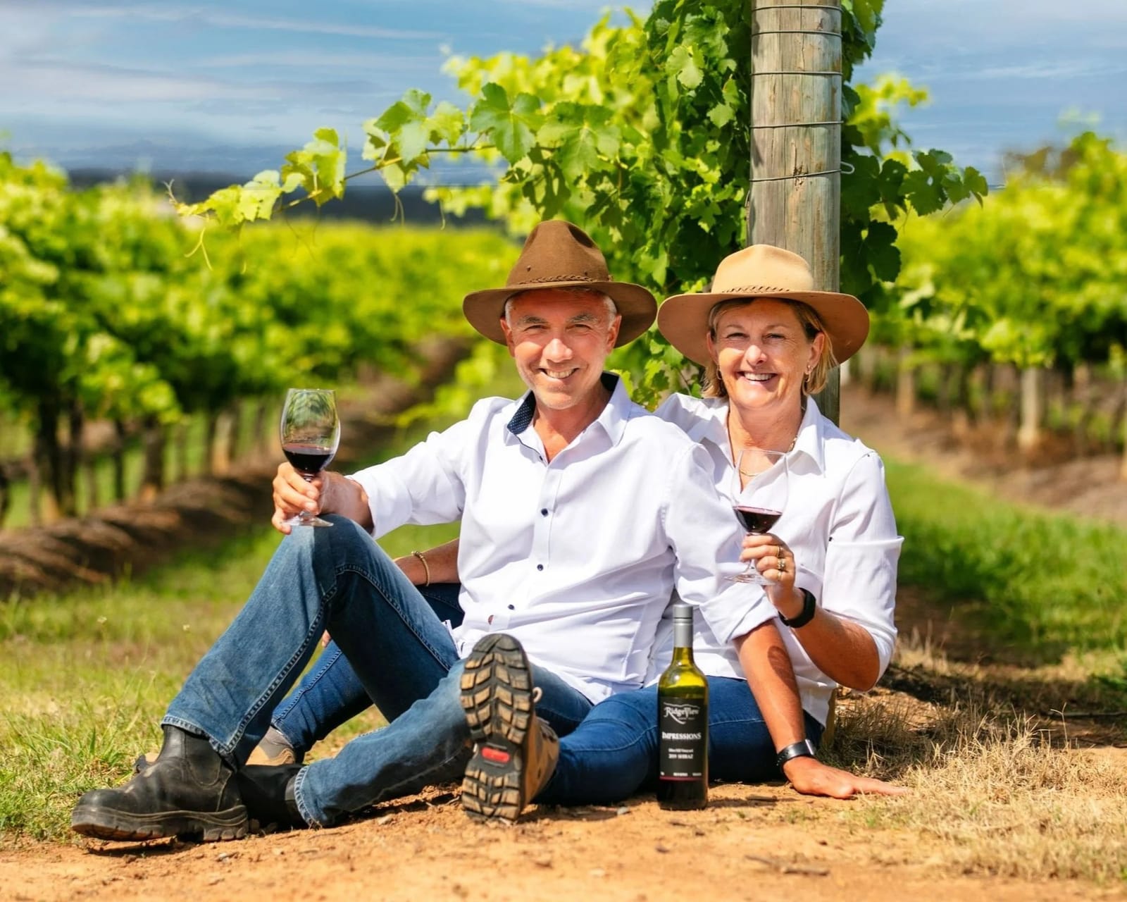 Vineyard owners holding wine glasses among grapevines at sunset