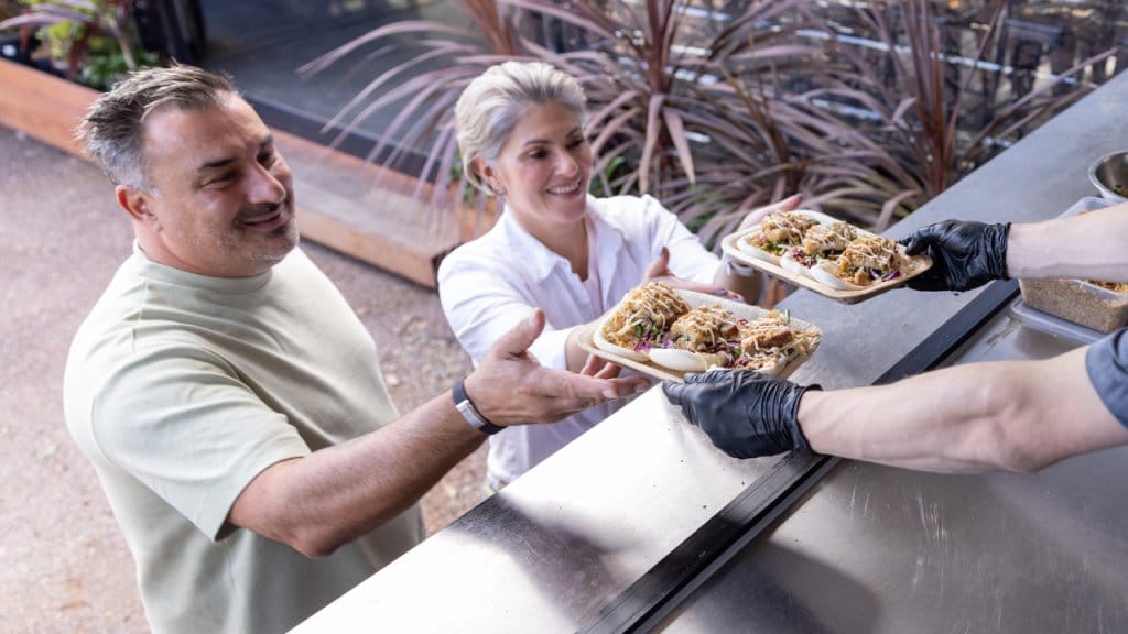 Staff serving food at outdoor counter window to customers