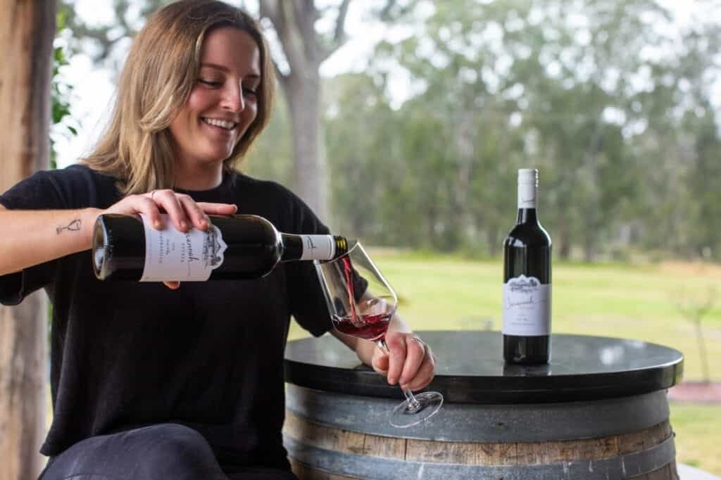 A staff member pouring red wine at a barrel table on the verandah