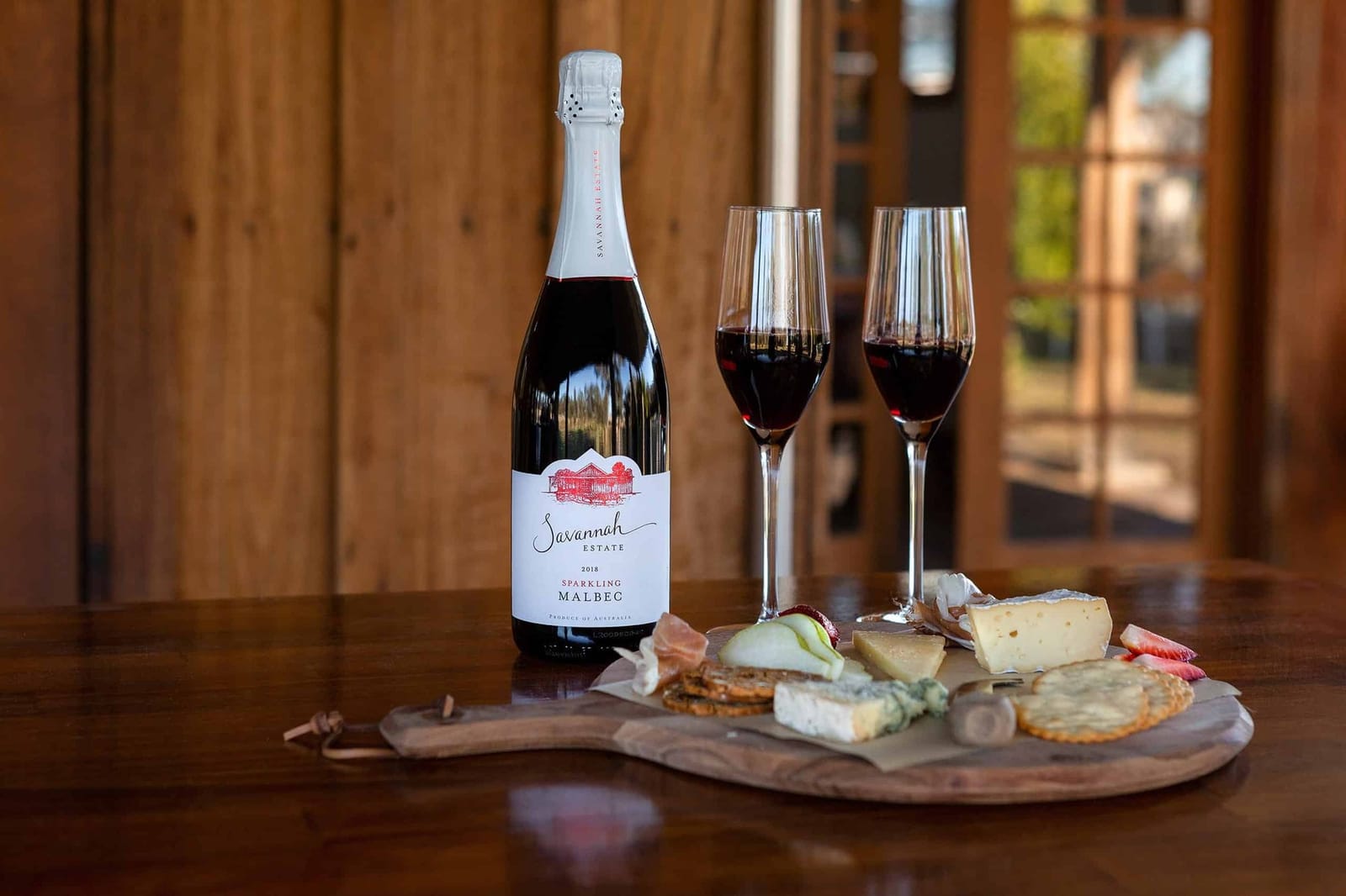 A bottle of Savannah Estate Sparkling Malbec with two glasses and a cheese board