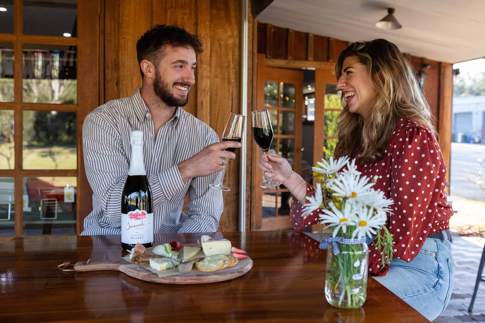Two guests toasting with red wine over a cheese board on the verandah