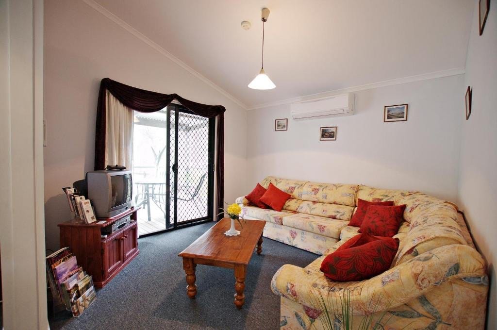 Living room with an L-shaped sofa, wall-mounted television and air conditioning unit.