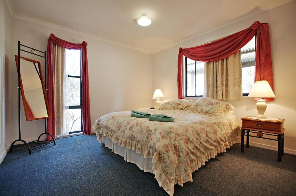 Queen bedroom with a freestanding dressing mirror and lace curtains at the window.