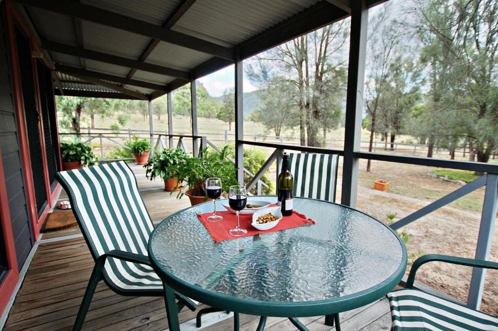 Verandah table set with wine and olives, looking out over paddocks toward the Upper Hunter hills.