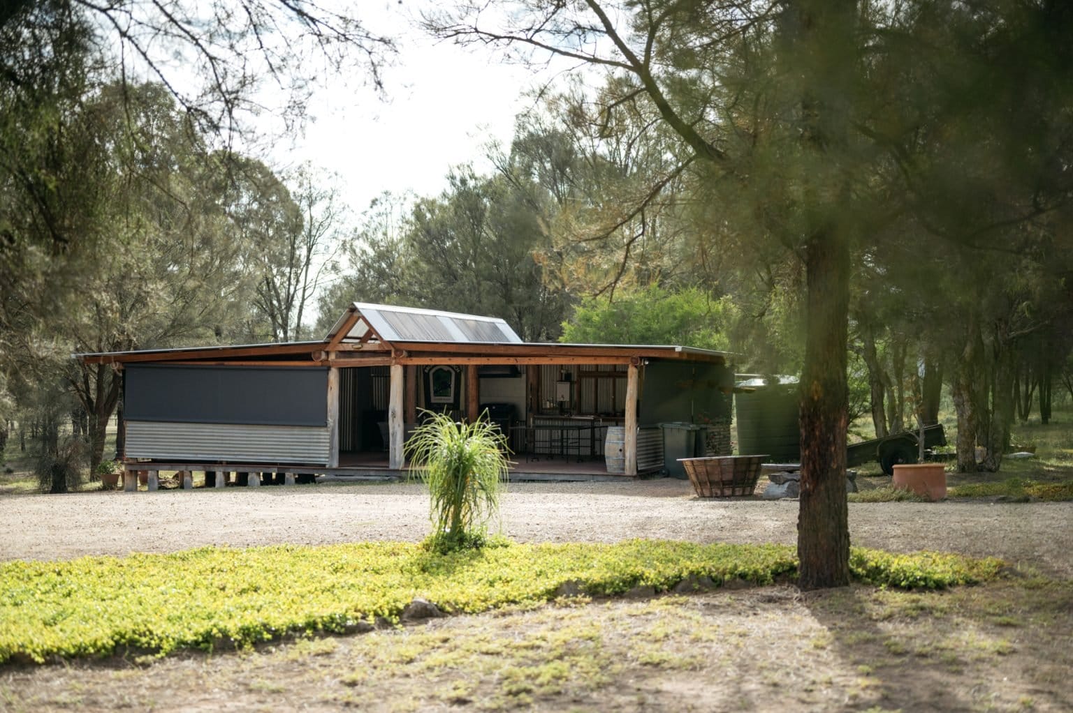 Covered outdoor kitchen and barbecue pavilion set among she-oak trees.