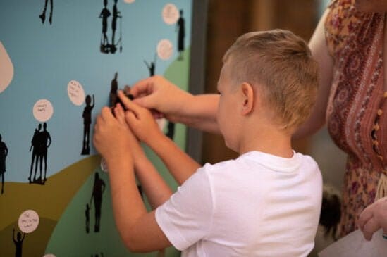 A child adding to an interactive display wall as part of a gallery activity, family looking on