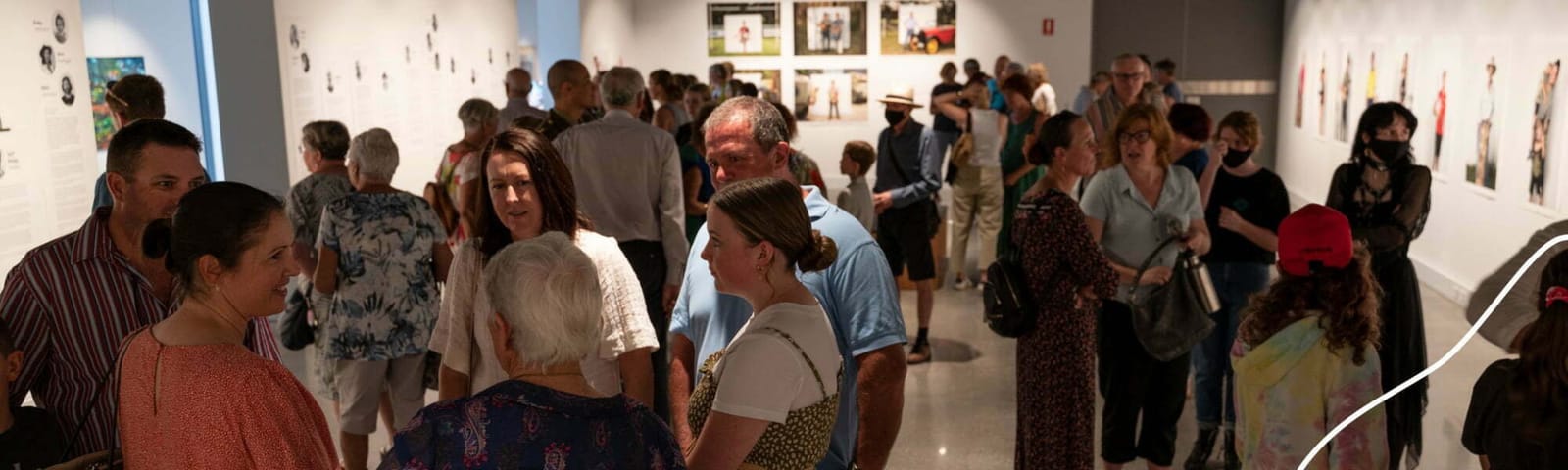 Visitors gathered inside the gallery at an exhibition opening, with framed works on the walls around them