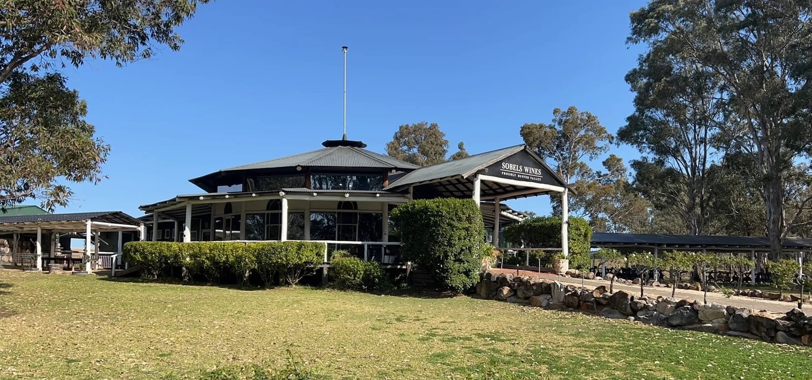 Single-storey building with wraparound veranda, lawn and trees at Sobels, Pokolbin, Hunter Valley