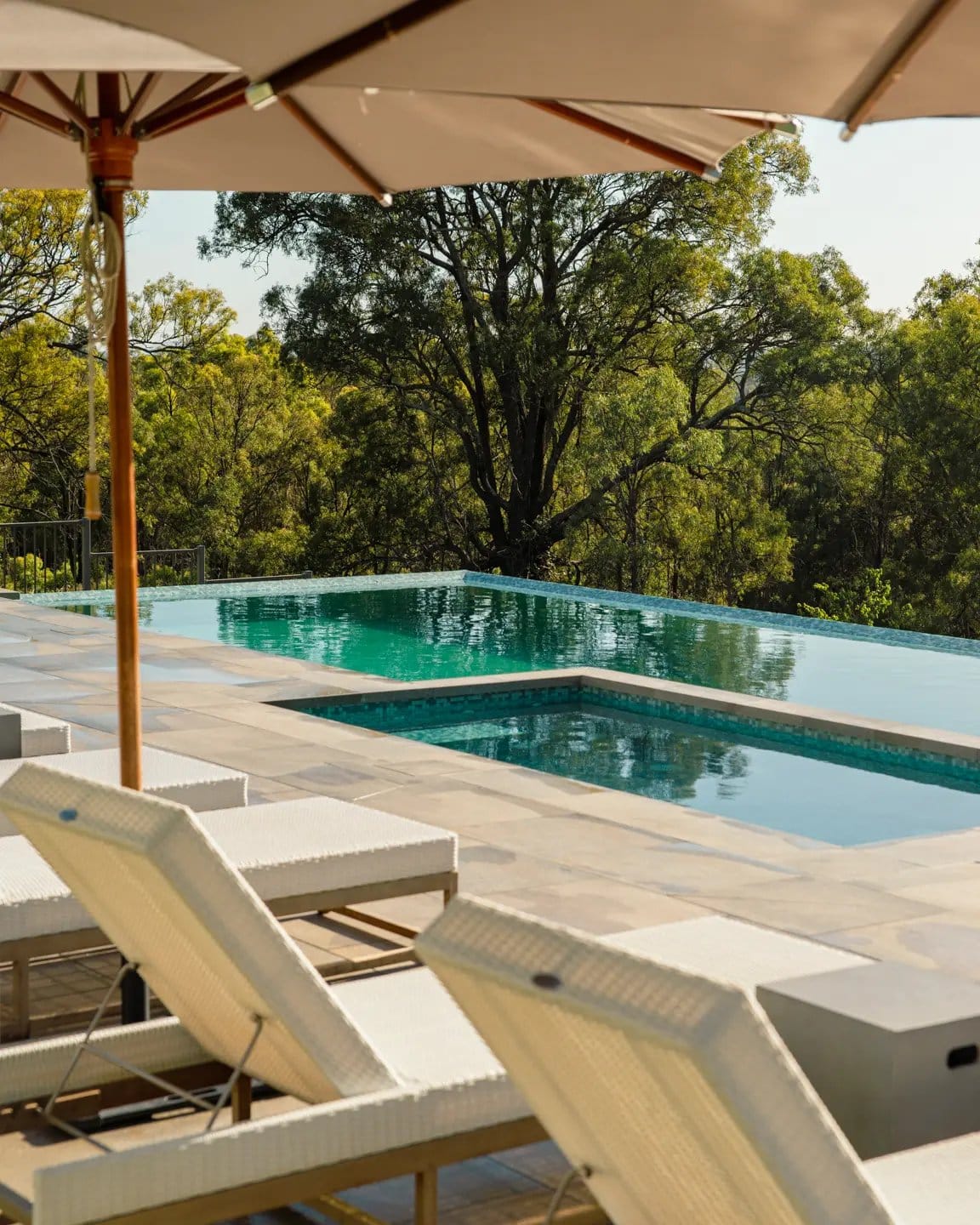 The pool and spa at Spicers Guesthouse, umbrellas and sun lounges beside them and bush beyond