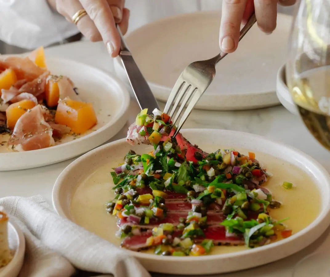 A plate of thinly sliced beef with salsa verde and capers being served at eRemo