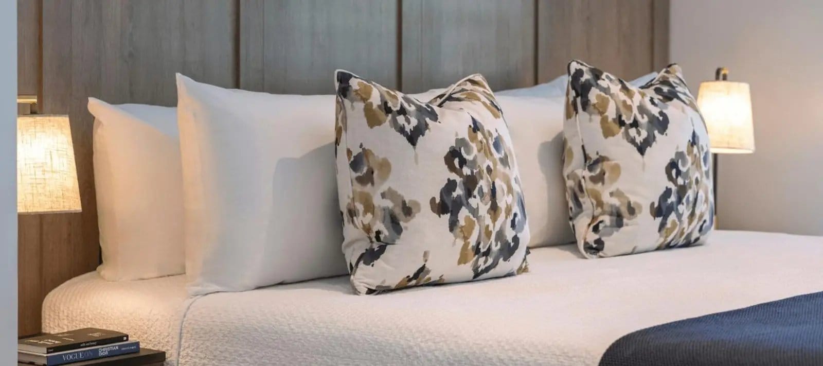 A made bed with white linen and patterned cushions against a timber headboard
