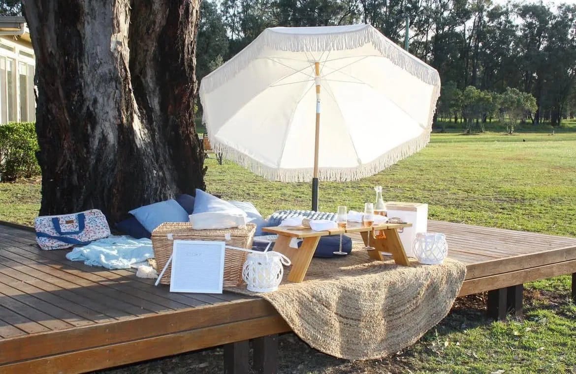 Outdoor picnic setup under fringed white umbrella with wine