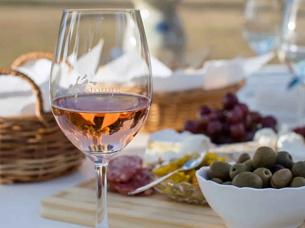 Rosé wine glass with cheese, grapes and olives on table