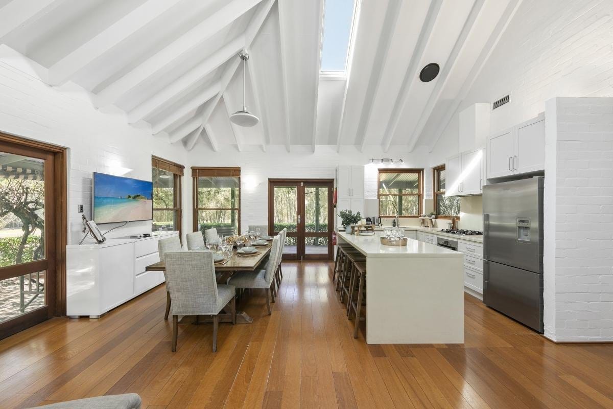 An open-plan white kitchen with island bench and dining table beyond