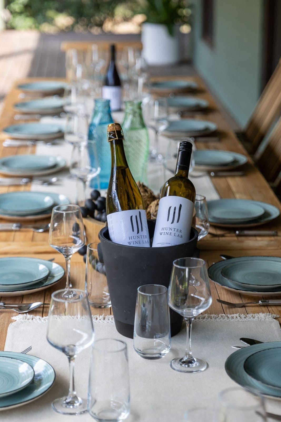 A long outdoor table set for a group dinner with wine and glassware