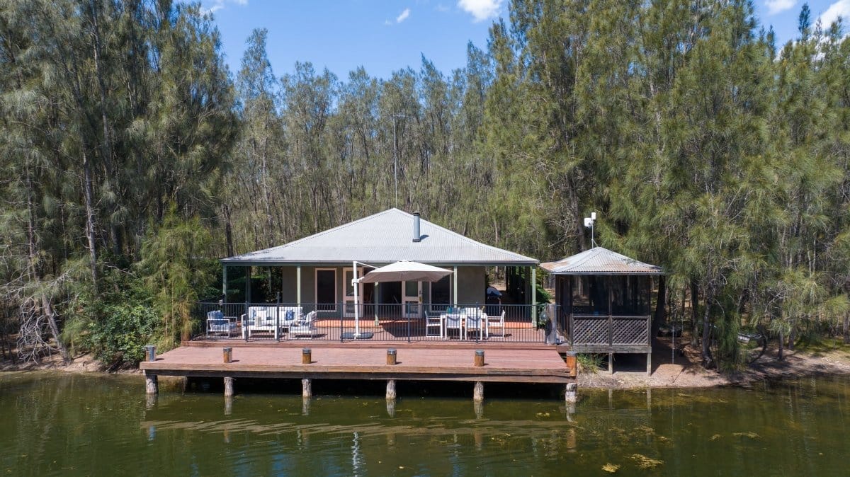 The Homestead deck extending out over the billabong, framed by casuarina trees