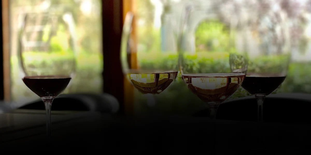 A flight of red and white wines in glasses on the tasting bench beside a window