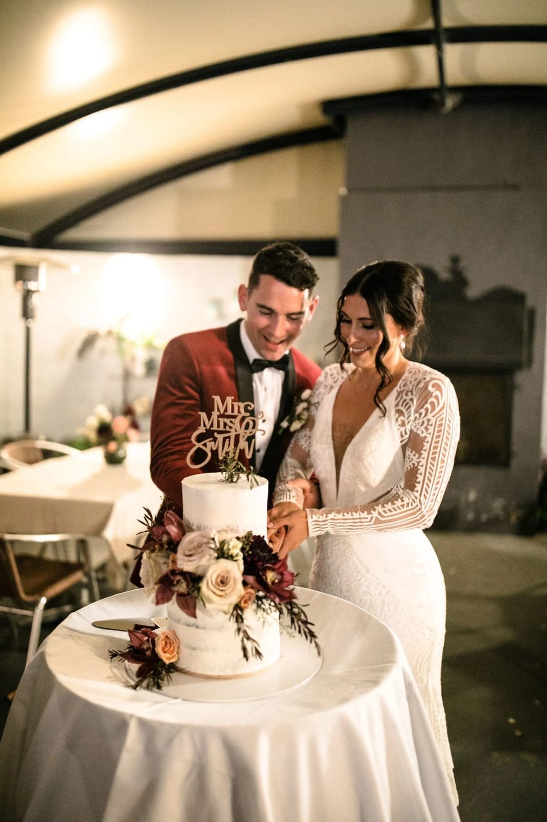 Couple cutting wedding cake indoors with modern lighting