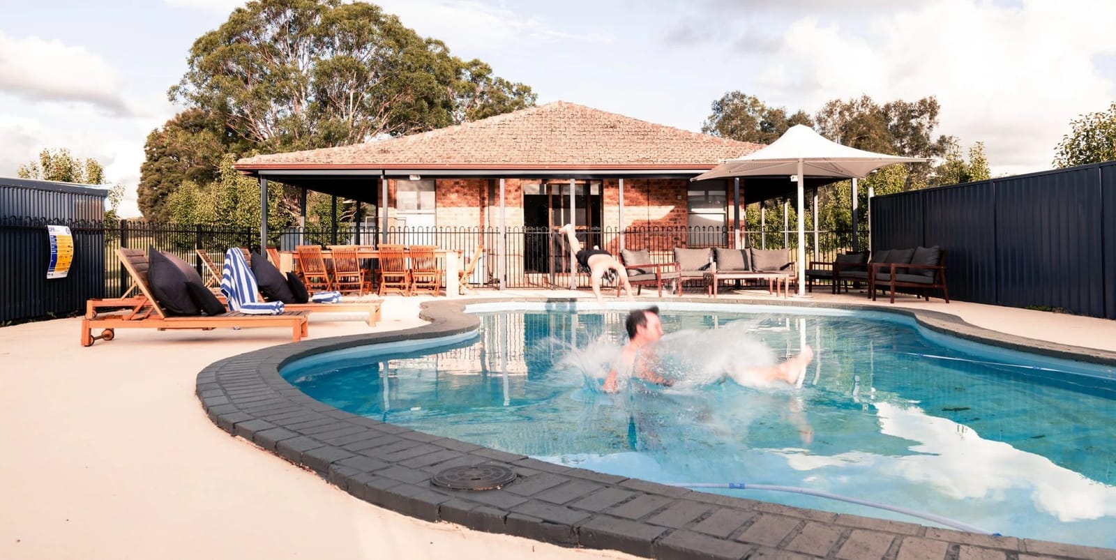 Swimming pool with heated spa and loungers near brick building