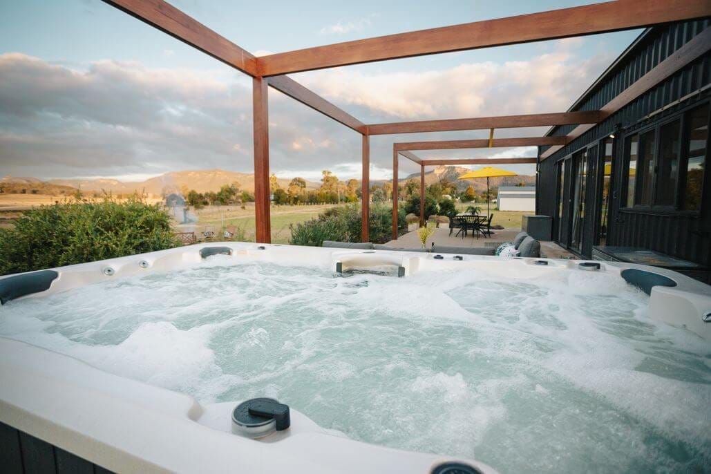 Heated spa bath under timber pergola with valley views