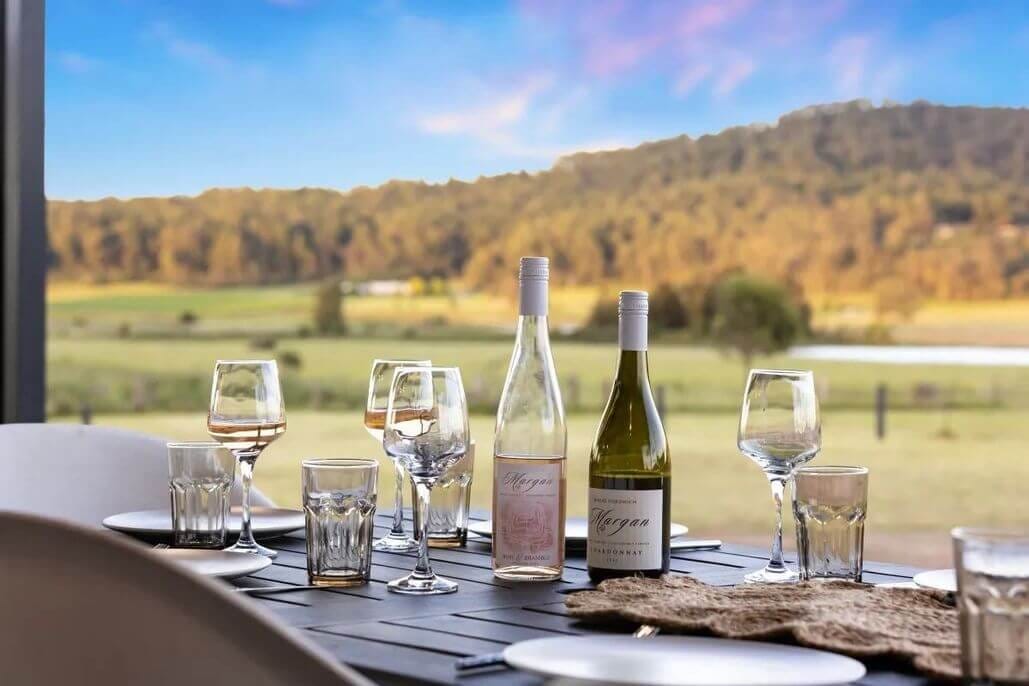 Wine bottles and filled glasses on table with landscape view