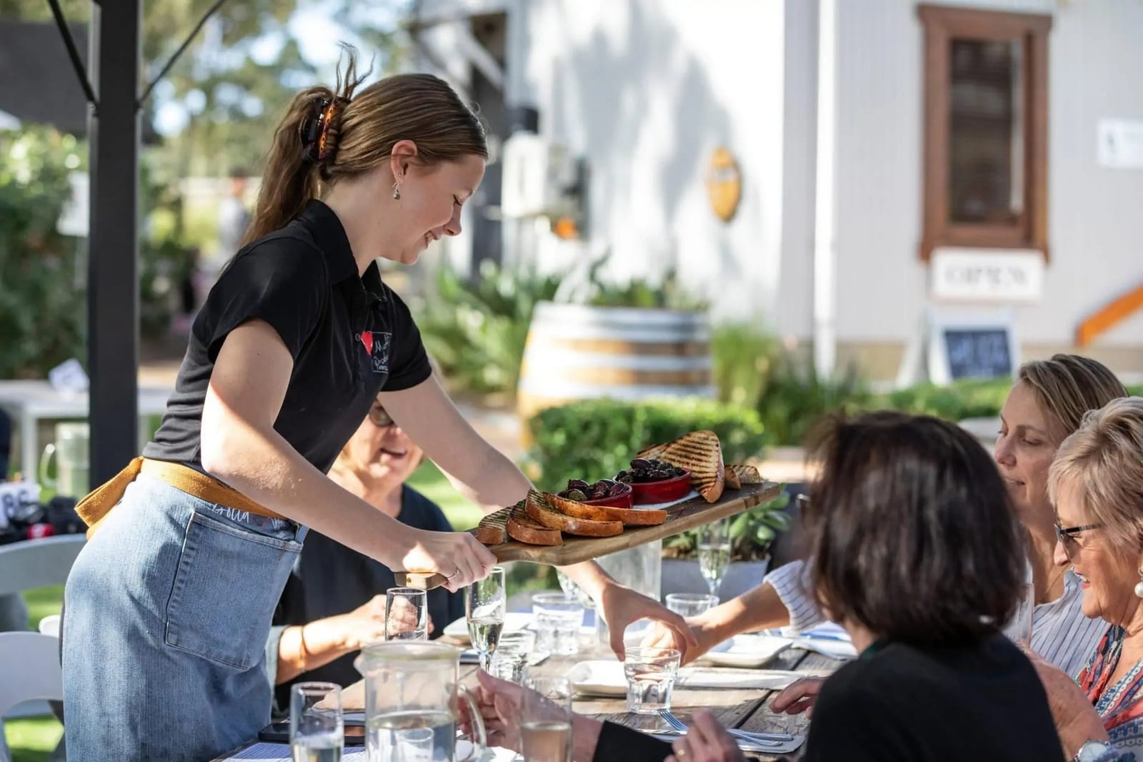Share board being carried to long outdoor table of diners at The Deck Cafe, Lovedale, Hunter Valley