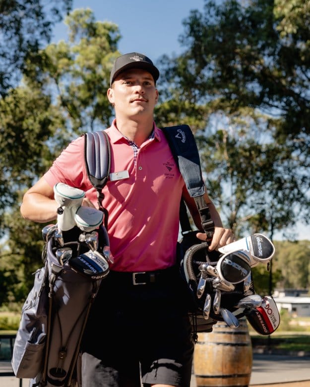 Male golfer holding clubs with trees and fairway in background at The Vintage Golf Club, Rothbury, Hunter Valley