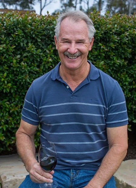 Man holding wine glass in vineyard with grapevines and paddocks