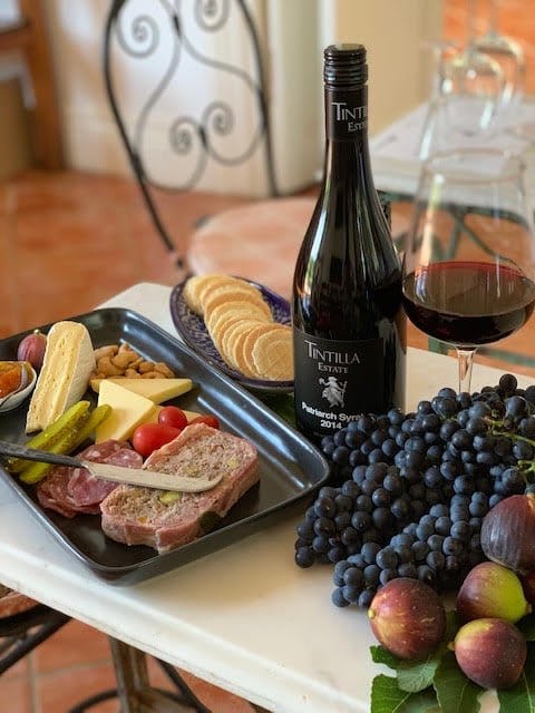A bottle of Tintilla Patriarch Syrah with a plate of cheese, terrine and olives